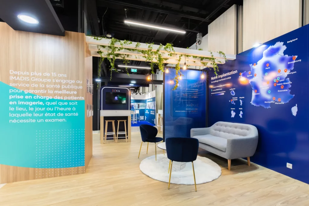 Photo d'un espace du stand IMADIS Groupe avec un canap&eacute; gris, deux fauteuils bleus, une table basse et un tapis blancs