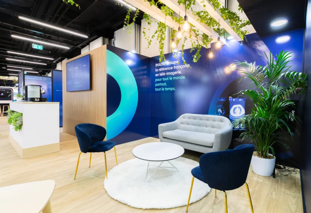 Photo d'un espace du stand IMADIS Groupe avec un canap&eacute; gris, deux fauteuils bleus, une table basse et un tapis blancs